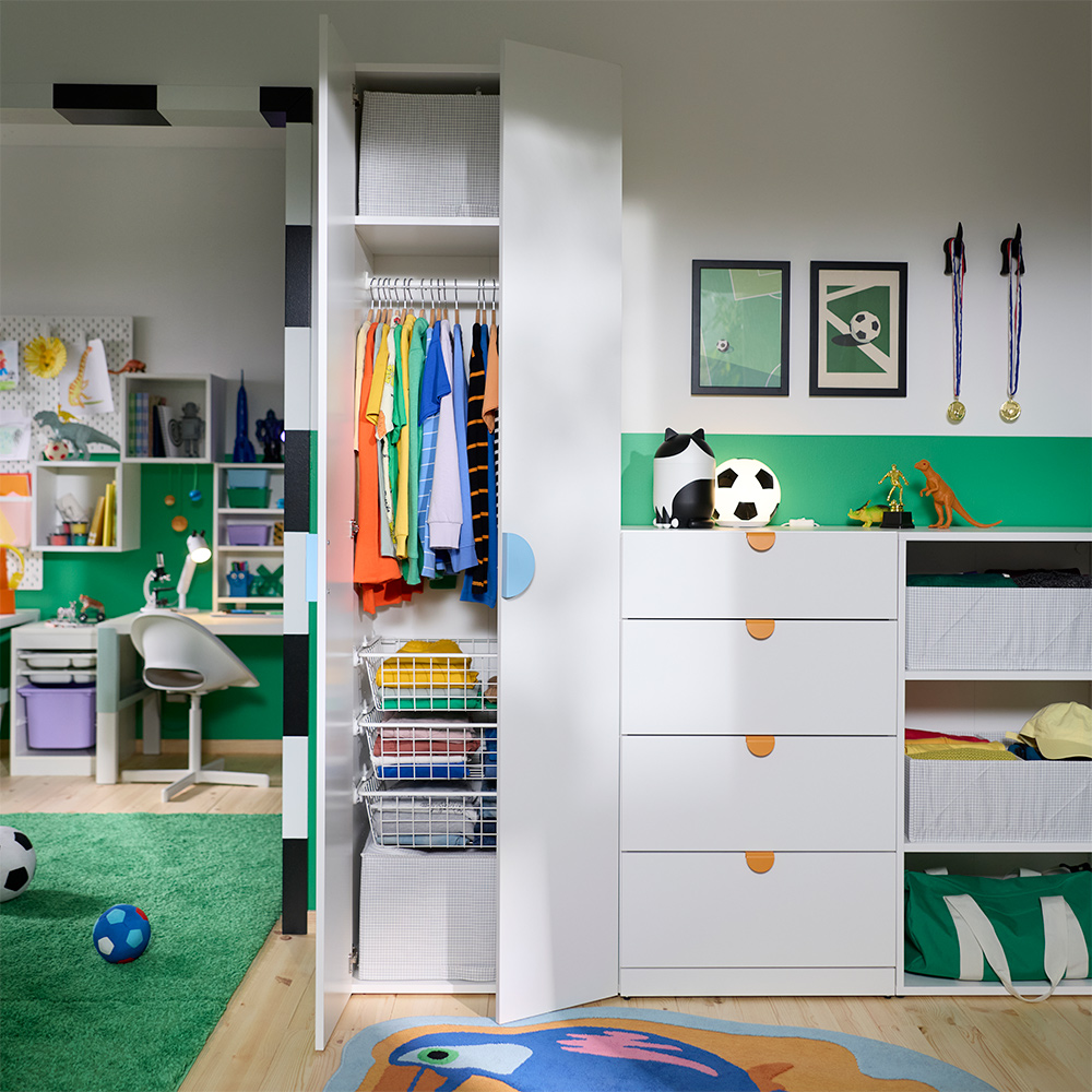 Una habitación infantil con una combinación de armario LASTARE con almacenamiento, barra para colgar y cajones, junto a un espacio de trabajo y una zona de juego.