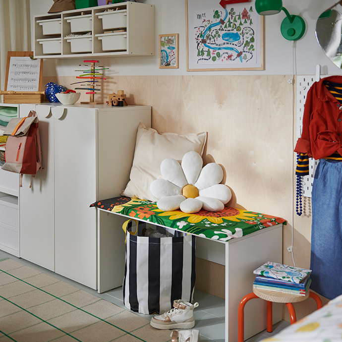 Una habitación infantil con una combinación de armario LASTARE, acompañada por un pequeño escritorio blanco y un cojín con forma de flor.