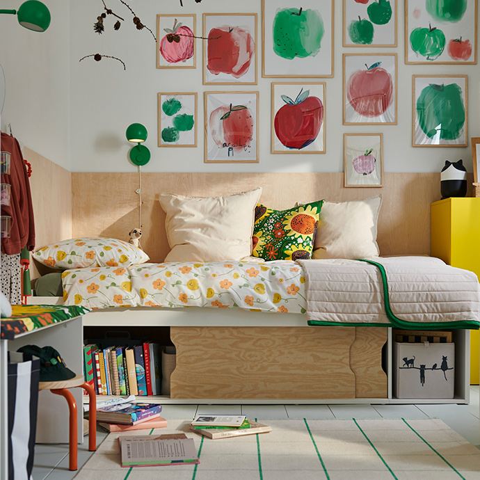 A bedroom with a white KLIPPUGGLA bed frame with storage beneath, dressed in colourful floral bedding and pillows.