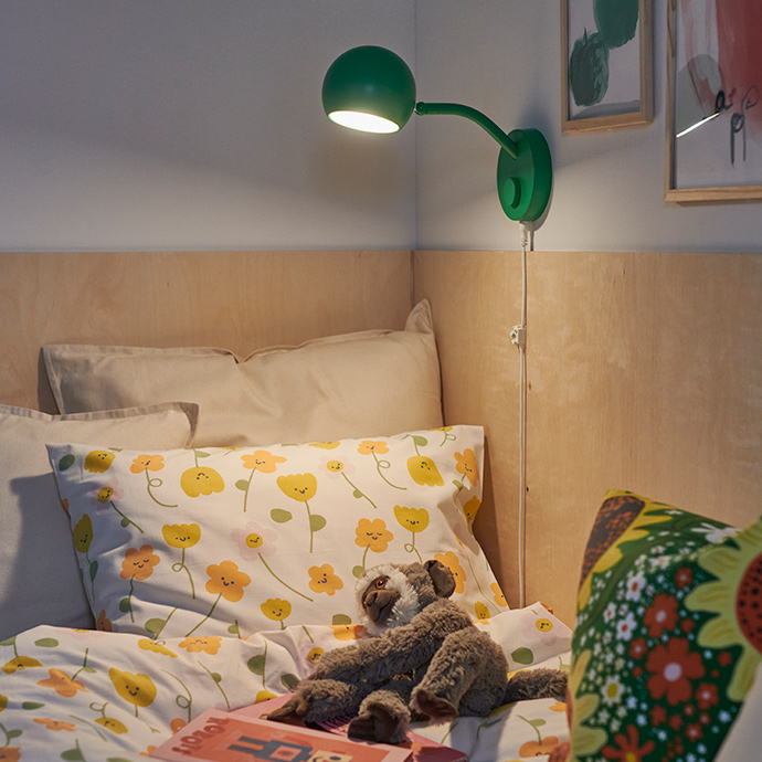 A bedroom featuring a green KORVSNÖRE lamp and a BARNDRÖM duvet cover set with a flower pattern, arranged on a bed.