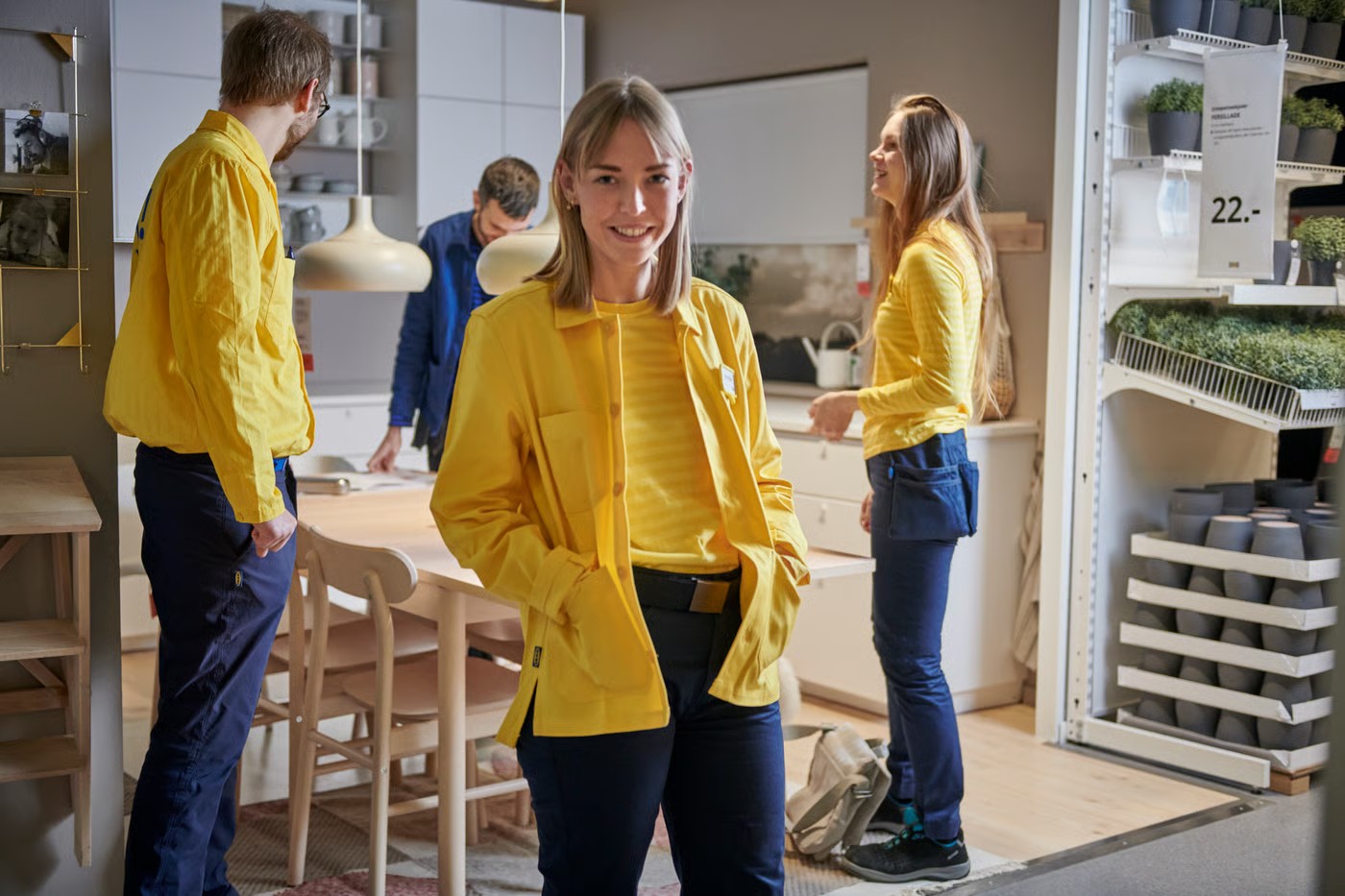 Several IKEA employees in yellow and blue uniforms smiling inside a store showroom section.