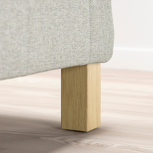 Somier de cama cubierto de tela gris claro con patas de madera clara.