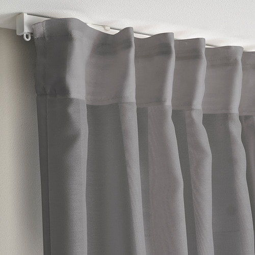 Las cortinas grises transparentes cuelgan con pliegues, difundiendo la luz del sol para mayor privacidad.