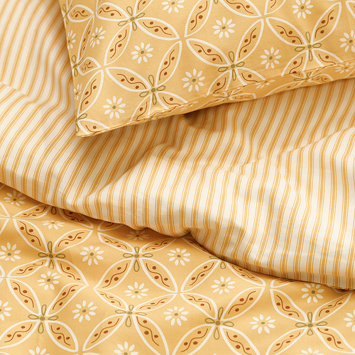Un primer plano de un conjunto de ropa de cama de color amarillo mostaza con un lado que muestra un patrón floral nostálgico y el otro a rayas.
