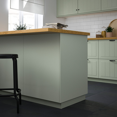 Cocina moderna con cubiertas de color verde claro, taburetes negros y encimera de madera.