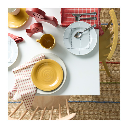 Platos y tazas de color amarillo brillante sobre manteles individuales a rayas, colocados sobre una mesa blanca con sillas rústicas.