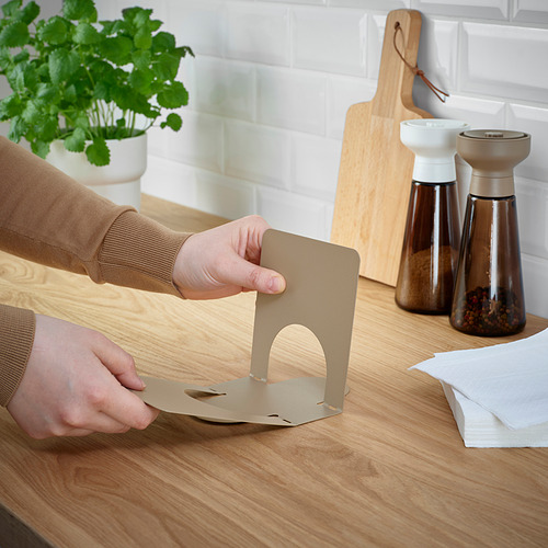 Montaje de servilletero beige en la mesa con condimentos, planta, tabla de cortar.