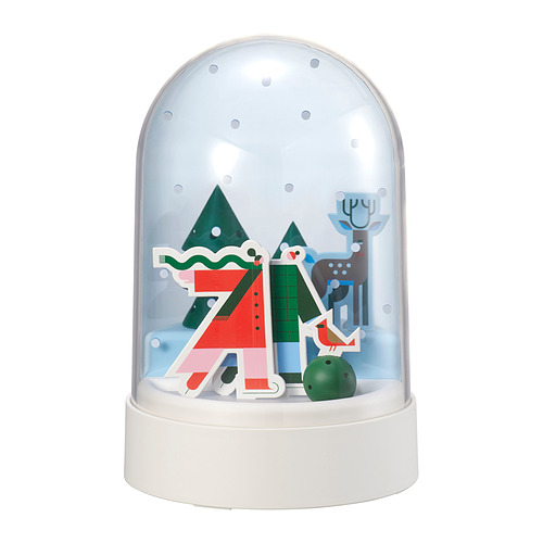 Lámpara de globo de nieve STRÅLA: base blanca, globo transparente, escena navideña con árboles rojos, verdes, renos y muñeco de nieve, iluminados cálidamente en el interior.