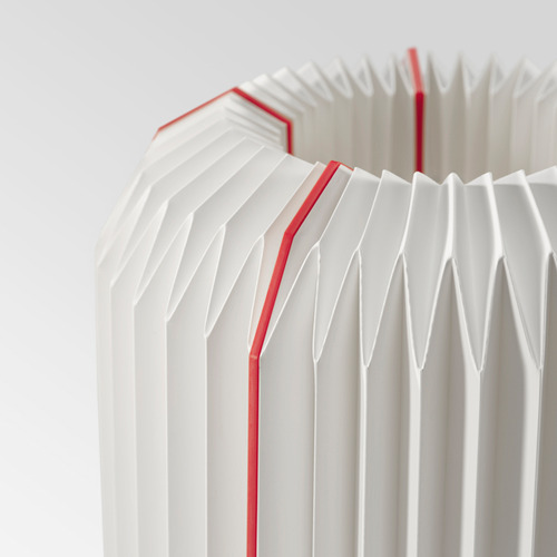 Lámpara moderna con pantalla plisada blanca con finas líneas rojas para un aspecto decorativo, que emite un resplandor cálido y acogedor.