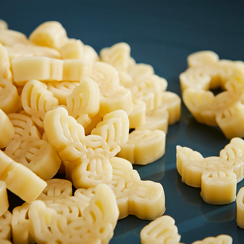 Pila de pasta amarilla con forma de alce sobre una superficie oscura. Höchst 150 caracteres.