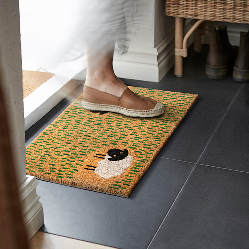 Una persona pisa un felpudo colorido con diseño de oveja, acogedor y práctico para el uso en interiores.