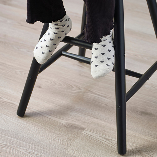 Un niño se sienta en una silla junior, con los pies en sus barras, vistiendo calcetines blancos con corazones negros. La silla proporciona la altura adecuada del asiento y el apoyo para los pies.