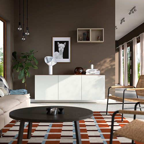 Salón moderno con aparador BESTÅ , lámpara, jarrón, libros, sofá beige, mesa de centro, alfombra, silla de mimbre, cuadro de alpaca y lámparas colgantes.