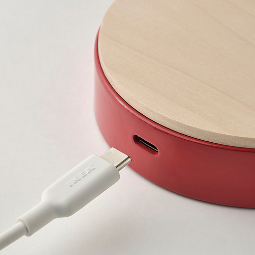 Se muestra una lámpara de escritorio roja con una tapa de madera y un puerto usb-c para cargar un dispositivo. Un cable USB-C blanco está conectado a la lámpara.