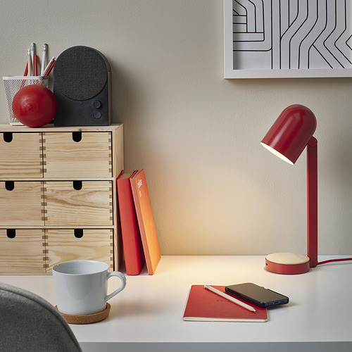 Lámpara de sobremesa ENSMÄRKE roja con base de madera, puerto usb-c, entre libros y cuaderno.