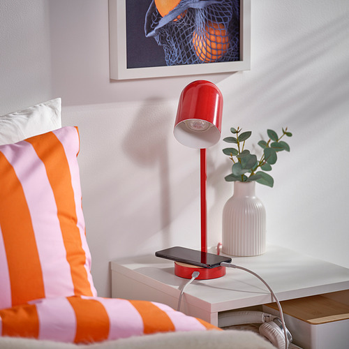 Lámpara de escritorio roja brillante con carga usb-c, iluminando el espacio de trabajo junto a almohadas de colores.