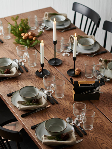 Mesa de comedor de madera con platos, vasos y cubiertos grises. Las velas y la vegetación decoran el centro. Cuatro sillas negras a su alrededor.