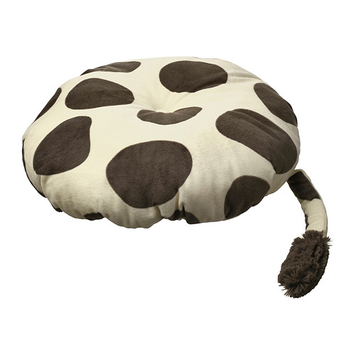 Un cojín con forma de jirafa, de color blanco con manchas marrones, hecho de suave poliéster reciclado, perfecto para un taburete infantil.