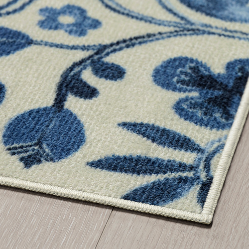 Alfombra floral azul y blanca con patrones intrincados, textura suave y afelpada, colocada sobre suelo de madera.