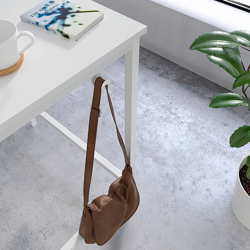 Escritorio blanco minimalista con bolsa marrón para colgar, planta, libro y taza.