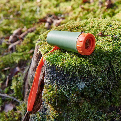 Mini monocular verde y naranja descansa sobre la rama de un árbol cubierta de musgo. Diseño duradero y compacto, ideal para uso en exteriores.