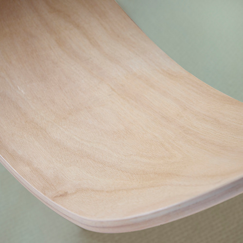 Tabla de equilibrio curva de madera clara, parte de la serie de muebles juguetones, expuesta sobre una superficie verde pálido.