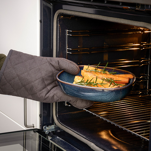 Persona usando guantes de cocina colocando un plato de cerámica azul con tubérculos en el horno, mostrando la funcionalidad del horno a la mesa de GLADELIG.