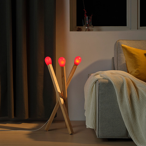 Acogedora sala de estar iluminada por una lámpara STRÅLA que se asemeja a cerillas de gran tamaño. La luz suave y regulable crea un ambiente cálido.