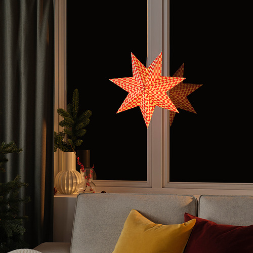Acogedora sala de estar con farol de estrella roja, sofá gris brillante con almohadas. Las plantas verdes y los jarrones dorados realzan el ambiente festivo.