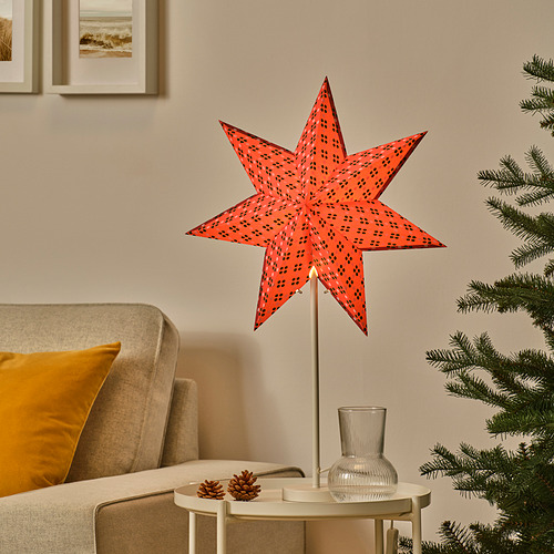 Lámpara de estrella STRÅLA de color rojo brillante, diseño de estrella de papel en 3D, iluminada, se sienta en la mesa junto al sofá, decoración de piña, jarrón, árbol de Navidad cerca.