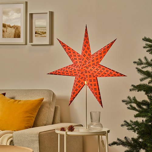 Lámpara de estrella roja STRÅLA sobre mesa con sofá y árbol.