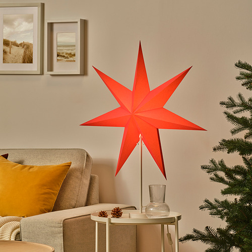 Lámpara de estrella roja brillante, grande y detallada, se encuentra alta sobre la mesa, rodeada de decoración navideña.