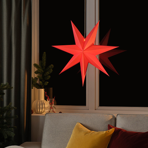 Una estrella de papel rojo brillante cuelga cerca de la ventana, más grande que las almohadas del sofá, lo que agrega una decoración festiva.