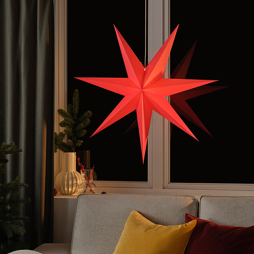 Acogedora sala de estar con decoración de estrella roja STRÅLA, gran ventana, sofá gris, almohadas amarillas, plantas y jarrones.