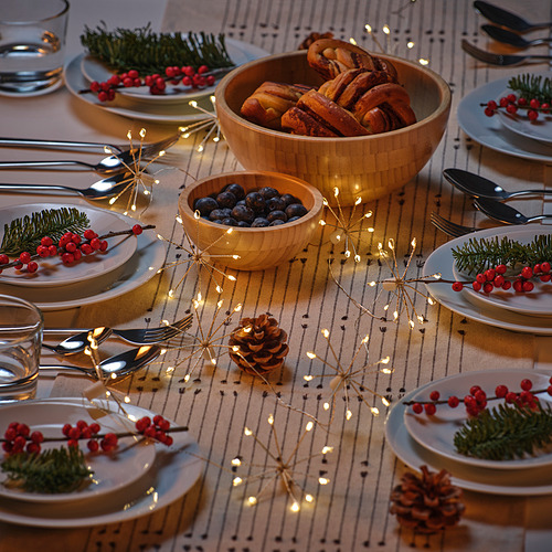 Mesa navideña con luces, platos, bayas y piñas STRÅLA. Ambiente cálido y chispeante.
