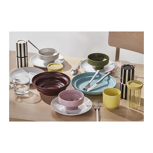 Una mesa con utensilios de cocina coloridos: tazas, cuencos, tarros en verde, amarillo, rosa y marrón, hechos de plástico y cristal, dispuestos con estilo.