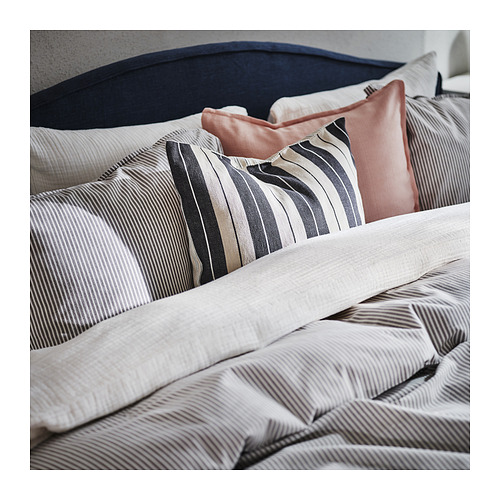 Cama con almohadas a rayas grises y blancas, una rosa, sobre un cabecero azul marino.