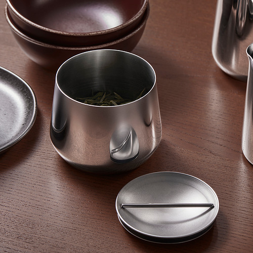 Un juego de cocina de acero inoxidable: cuencos, tetera, tarro con té verde sobre madera. O, para menos personajes: juego de cocina de acero inoxidable con tarro de té sobre madera.