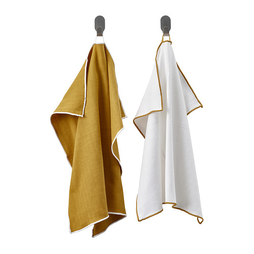 Dos paños de cocina mostaza y blancos con bordes en bucle cuelgan de ganchos.