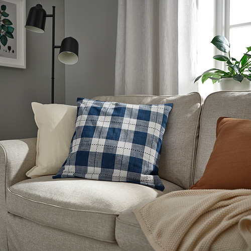 Acogedora sala de estar con sofá de color claro, almohada a cuadros, lámpara y planta de interior.