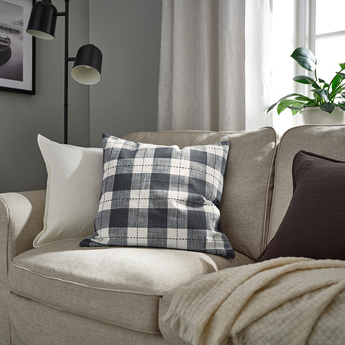 Sofá beige con cojín de cuadros SVAMPFLY, almohadas, planta y lámpara.