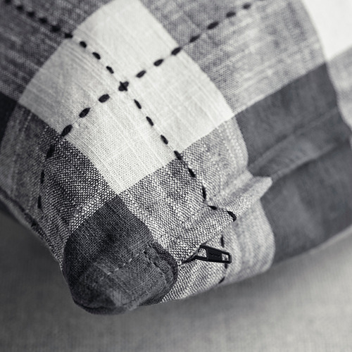 En blanco y negro, una funda de cojín con un patrón de cuadros tradicional, con costuras visibles y una cremallera.