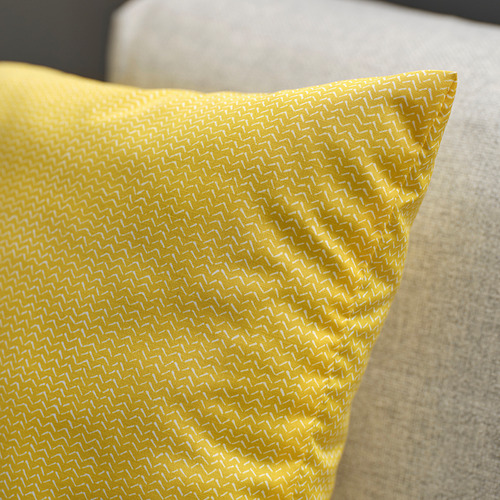 Cojín amarillo brillante con un intrincado patrón tejido, colocado sobre una superficie beige suave.