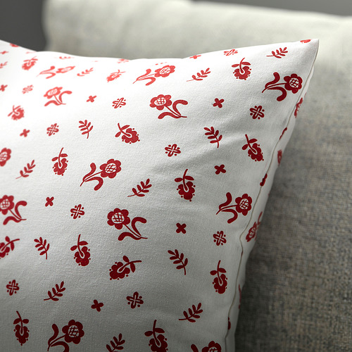 Cojín blanco con motivos florales rojos, colocado sobre una textura gris.