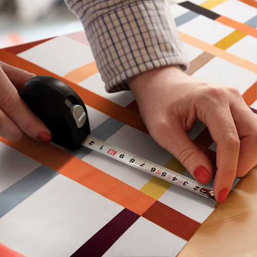 La persona usa la regla sobre una tela de cuadros coloridos junto a un ratón, planificando un proyecto de costura.