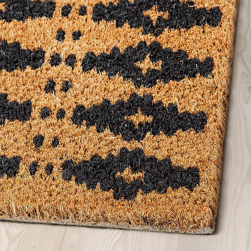 Felpudo con estampado negro y fuego sobre suelo de madera, hecho a mano con fibras de coco gruesas y texturizadas.