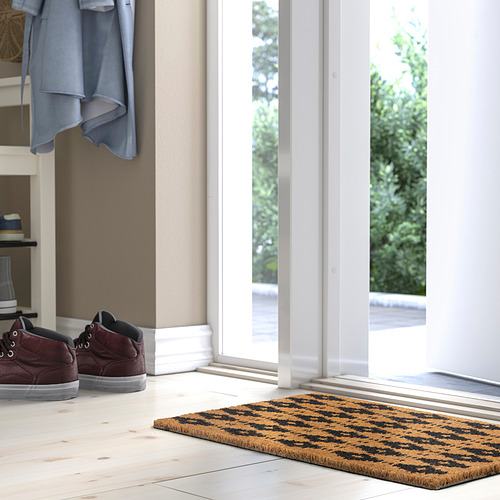 Entrada moderna con alfombra BETALVÄG, patrón geométrico, puerta grande, casi de vidrio, zapatillas rojas, chaqueta azul.