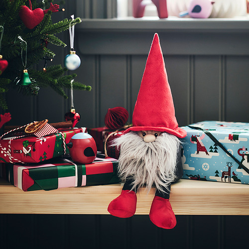 Un festivo peluche de Santa Claus rojo VINTERFINT se sienta en los estantes, más pequeño que los regalos envueltos y rodeado de decoraciones navideñas.