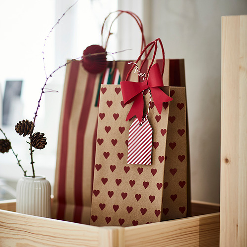 Dos bolsas de regalo con motivos de corazones y lazos rojos, una grande y otra mediana, colocadas en una caja de madera con un pequeño jarrón que contiene flores secas.