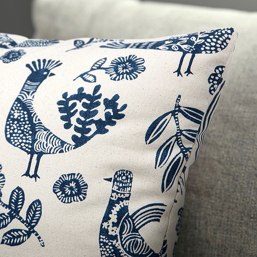 Cojín decorativo con pájaros azules y motivos florales en algodón blanco roto, costuras detalladas, cremallera oculta.